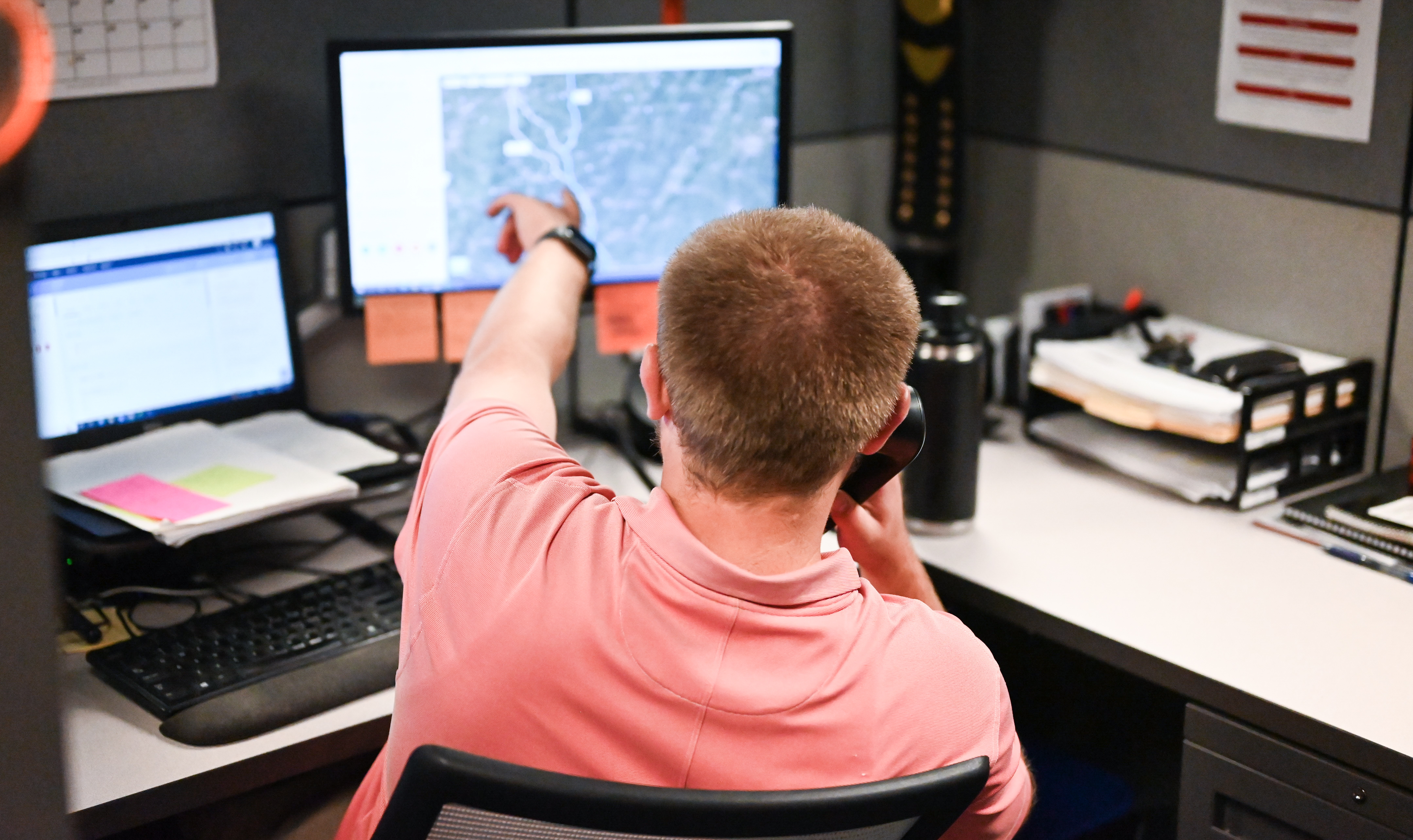 Logistics expert talks on office phone while pointing to his computer screen.