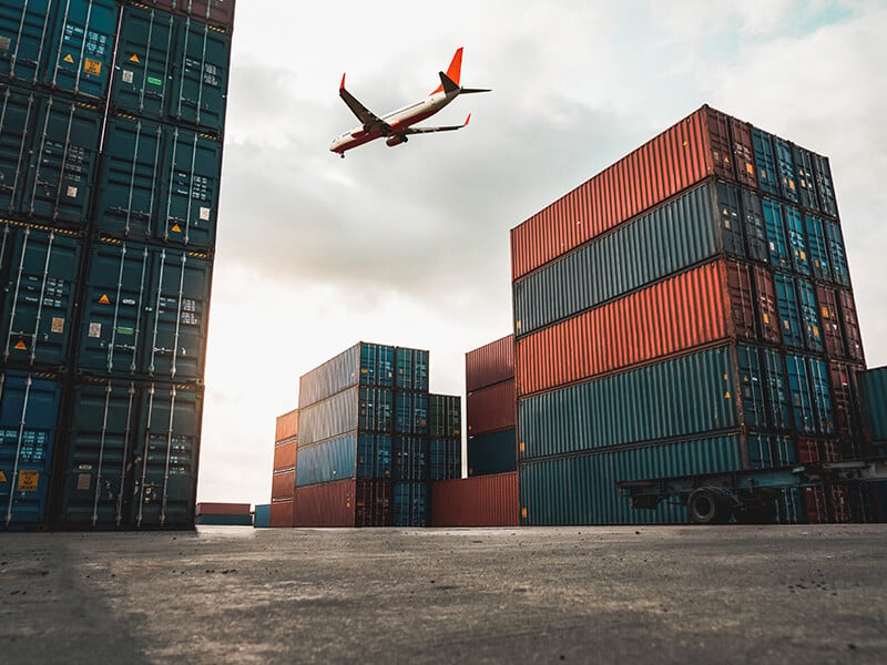 Freight airplane flying above overseas shipping container