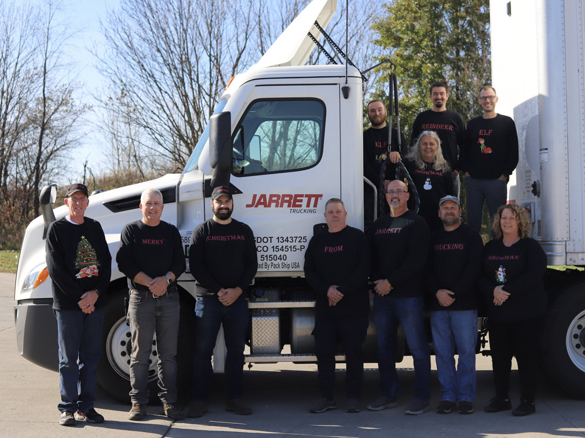 Jarrett team wearing christmas sweaters stand in front of semi truck