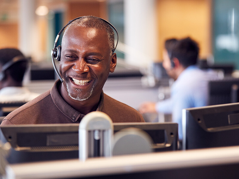 Mature Businessman Wearing Telephone Headset Talking To Caller In Customer Services Department