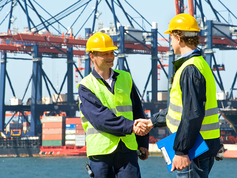 Two dock workers shaking hands in a shipping yard