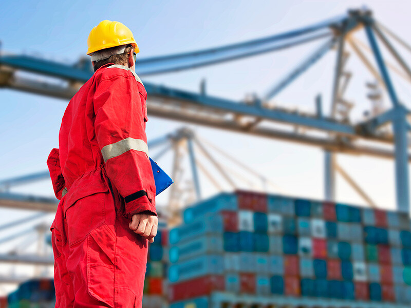 Worker standing and looking at a ship with containers